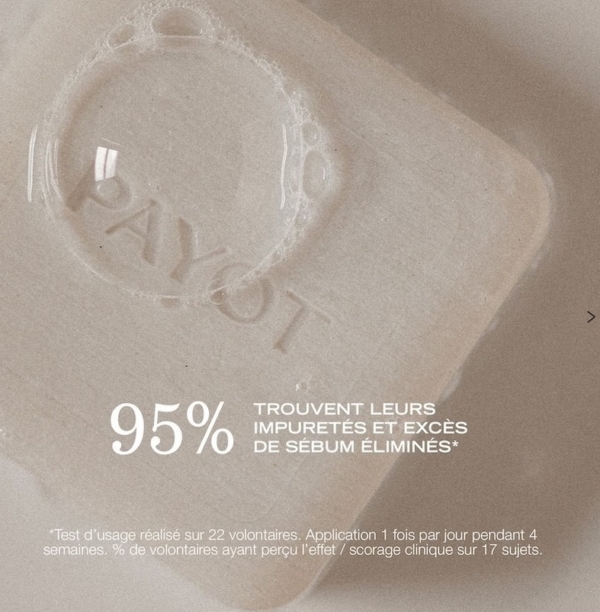 Un pain beige Payot Savon Nettoyant Purifiant Anti Imperfections Visage et Corps de 65 g avec "PAYOT" gravé repose sur un fond neutre surmonté d'une bulle de savon. Le texte français indique que 95 % des personnes ont observé moins d'impuretés et d'excès de sébum après utilisation. Dakar