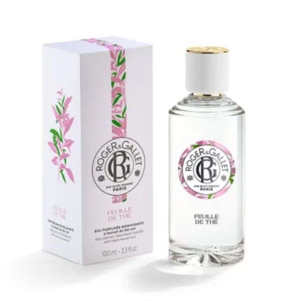 Un flacon transparent de Roger et Gallet Feuille de Thé Eau de parfum 100ML avec un bouchon blanc et une étiquette ronde en texte noir se trouve à côté de sa boîte florale blanche et rose. Dakar