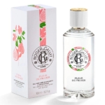 Un flacon du parfum Roger & Gallet Fleur de Figuier se trouve à côté de sa boîte blanche décorative, qui comporte des illustrations de fleurs roses et de figues. Le flacon a un corps transparent, un bouchon doré et une étiquette assortie au design du coffret. Dakar