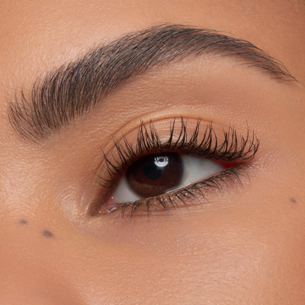 Gros plan sur l'œil d'une personne aux sourcils bien dessinés, aux longs cils recourbés grâce à la Base de Mascara Fixatrice de Boucles Cils 7 ml d'Essence, à la peau lisse, à deux petits grains de beauté sous l'œil et au maquillage naturel et subtil. Dakar