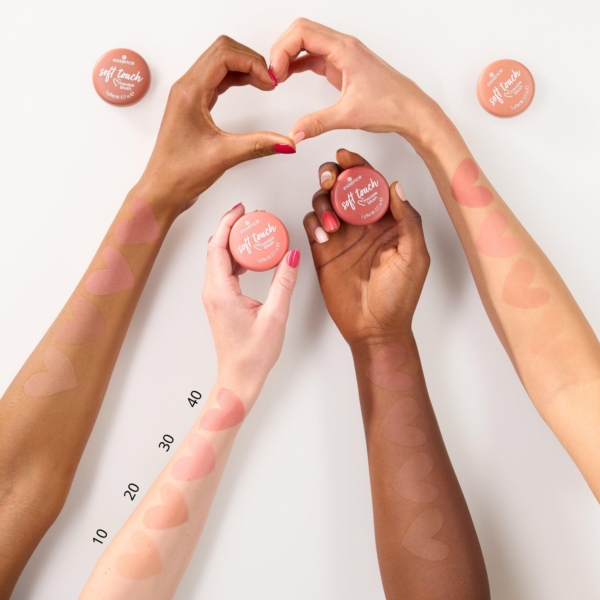 Quatre bras de différentes couleurs de peau montrent des échantillons de fard à joues en forme de cœur. Deux mains forment un cœur et deux tiennent des contenants de fard à joues étiquetés "Soft Touch Blush". Les numéros 10, 20, 30 et 40 sont indiqués sur un bras. Dakar