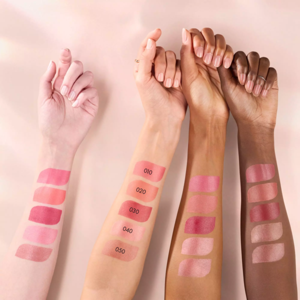 Trois bras aux teints variés présentent des échantillons de Catrice Blushin' Charm Multi Stick Blush en Stick 5,5 g dans cinq teintes roses - 010, 020, 030, 040 et 050 - sur leurs avant-bras sur un fond clair. Dakar