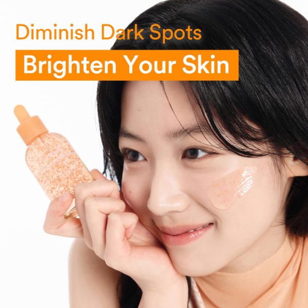 Une femme sourit en appliquant Abib Sérum Éclaircissant Glutathiosome Dark Spot 50 ml sur sa joue à partir d'un flacon compte-gouttes avec des particules orange. Texte : "Atténuez les taches brunes, illuminez votre peau. Dakar