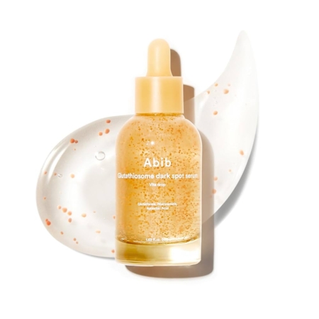 Un flacon compte-gouttes transparent étiqueté "Abib Sérum Éclaircissant Glutathiosome Dark Spot 50 ml", rempli de sérum jaune translucide et de minuscules billes orange, est posé sur un frottis texturé du même sérum sur un fond blanc. Dakar