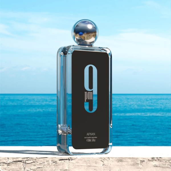 Afnan 9 PM Eau de Parfum pour Homme 100ml dans un flacon en verre transparent est posé sur du béton avec l'océan et le ciel bleus en arrière-plan. Dakar