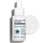 Un flacon compte-gouttes blanc de Aplb Sérum Ampoule Anti Taches à l'Acide Tranexamique et Niacinamide 40 ml est représenté à côté d'une goutte ronde de liquide clair sur un fond blanc. Dakar