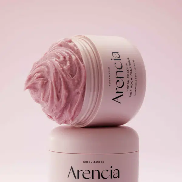 Le Mochi Soin 3 en 1 Nettoyant Exfoliant et Masque 120 g d'Arencia Fresh Rosehip Rice déborde d'un pot rond ouvert, empilé sur un récipient fermé assorti, sur fond de rose tendre. Dakar