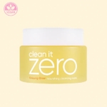 Un pot jaune de Banila Co Baume Nettoyant et Démaquillant Nourrissant Clean It Zero 100 ml avec un couvercle blanc, un texte blanc en gras et un symbole végétalien dans le coin supérieur gauche se trouve sur un fond beige clair. Dakar