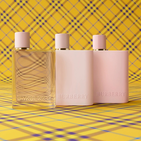 Trois flacons Burberry Her Eau de Parfum pour Femme 50ml - l'un transparent, les deux autres rose pastel - se dressent devant un fond écossais jaune, créant une présentation chic et coordonnée. Dakar