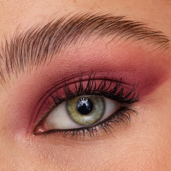 Gros plan sur un œil vert avec une ombre à paupières rose et bordeaux, un liner foncé utilisant le Catrice Crayon Yeux Contour Interne Inside Eye Khol Kajal 0,3 g, de longs cils et des sourcils bien dessinés. Dakar
