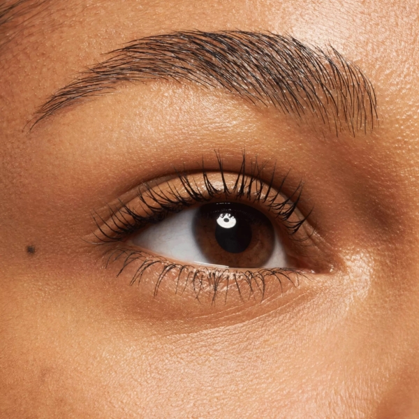 Gros plan sur un œil brun aux longs cils rehaussés par le Mascara Effet Faux Cils Glam&Doll False Lashes 9,5 ml de Catrice, un sourcil bien dessiné, une peau lisse et un petit grain de beauté sous l'œil. Dakar