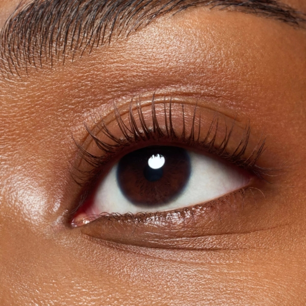 Gros plan sur un œil brun aux longs cils et aux sourcils parfaitement dessinés, mettant en valeur l'effet volumineux du Mascara Catrice Waterproof Glam&Doll Volume Longue Tenue Brown 10 ml sous un éclairage naturel. Dakar
