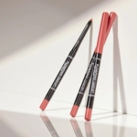 Trois Catrice Plumping Lip Liner Crayon Lèvres Repulpant Longue Tenue 0.35g corail sont présentés sur une surface blanche - deux adossés à un mur et un debout, tous projetant des ombres douces. Dakar