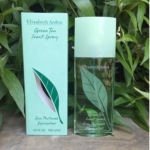 Un flacon et une boîte d'Eau de Parfum Elizabeth Arden Green Tea 100ml, avec un emballage sur le thème des feuilles vertes et blanches, présentés à l'extérieur parmi des feuilles vertes. Dakar