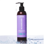 Un flacon pompe marron avec une étiquette violette "IN HAIRCARE milk in" se trouve sur un fond blanc, des gouttes d'eau sur sa surface et un goutte-à-goutte au niveau de l'embout - mettant en évidence le rafraîchissant In HairCare Leave-in Milk' In Définit les Boucles, Hydrate et Fortifie (250ml). Dakar