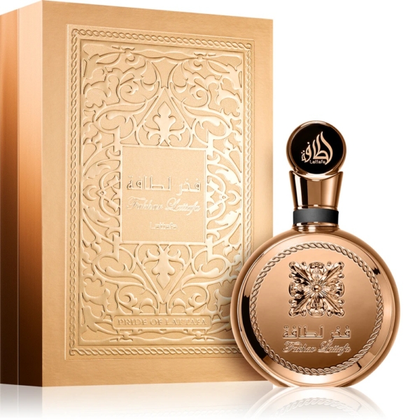 Le flacon doré de Lattafa Fakhar Lattafa Extrait Eau de Parfum pour Homme 100ml, orné de détails en relief et d'écritures arabes, se trouve à côté de l'élégant coffret assorti, tous deux respirant le luxe et la sophistication. Dakar