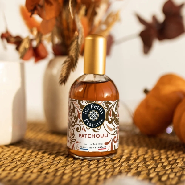 Un flacon de Les Petits Plaisirs Eau de Toilette Patchouli 110 ml est posé sur une surface tissée, avec en arrière-plan des fleurs séchées d'automne et des petites citrouilles, légèrement floues. Dakar