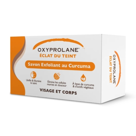 Une boîte blanche et orange d'Oxyprolane Savon Exfoliant au Curcuma Éclat du Teint 220 g met en valeur le curcuma et les extraits de plantes pour les soins du visage et du corps, en soulignant ses bienfaits exfoliants. Dakar