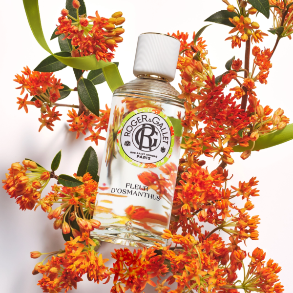 Un flacon de parfum Roger & Gallet Fleur d'Osmanthus est entouré de fleurs d'osmanthus orange vif et de feuilles vertes sur un fond blanc. Dakar