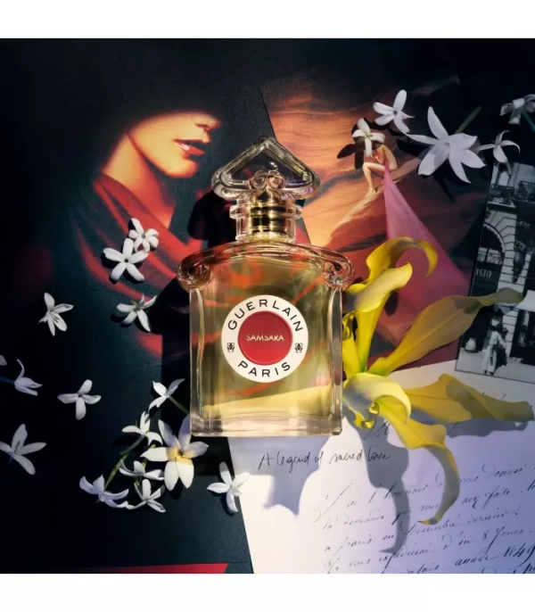 Un flacon de parfum Guerlain Paris Samsara repose sur des papiers colorés parsemés de fleurs blanches et jaunes, une photo vintage et une lettre manuscrite, créant ainsi une atmosphère romantique et élégante. Dakar