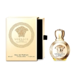 Un coffret en or et un flacon rond de Versace Eros Pour Femme 50ml, tous deux ornés du logo de la Méduse et du motif de la clé grecque. Le flacon est muni d'un bouchon en or, tandis que la boîte partiellement ouverte se trouve à côté. Dakar