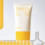 Un tube de crème solaire celimax Pore + Dark Spot Brightening Care avec SPF 50+ est présenté à la verticale sur un fond clair, avec un emballage jaune et blanc. Des objets en verre et un élément jaune sont partiellement visibles à proximité. Dakar