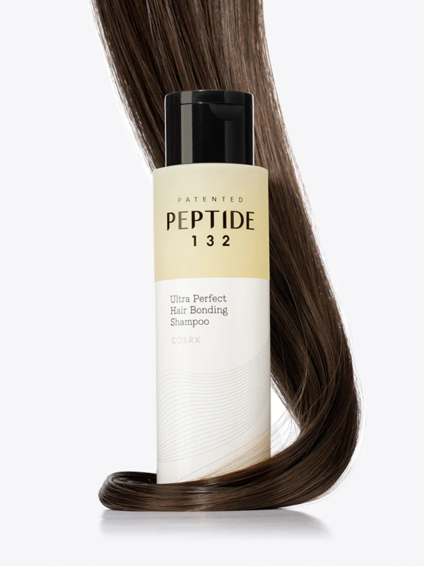 Un flacon de shampooing COSRX Peptide 132 Ultra Perfect Hair Bonding Shampoo est représenté avec des cheveux bruns lisses et brillants enroulés autour de sa base sur un fond blanc. Dakar