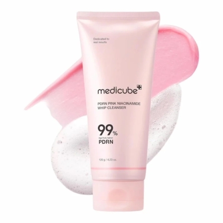Un tube rose de Medicube PDRN Pink Niacinamide Whip Cleanser se tient debout devant des échantillons de mousse rose et blanche. L'étiquette met en évidence 99 % de PDRN et de niacinamide sur un fond blanc. Dakar