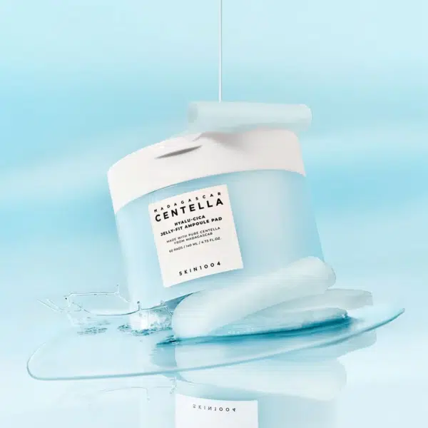 Un pot bleu clair de tampons nettoyants SKIN1004 Madagascar Centella est posé sur une flaque d'eau entourée de glaçons. Le liquide est versé sur le pot sur un fond bleu clair. Dakar