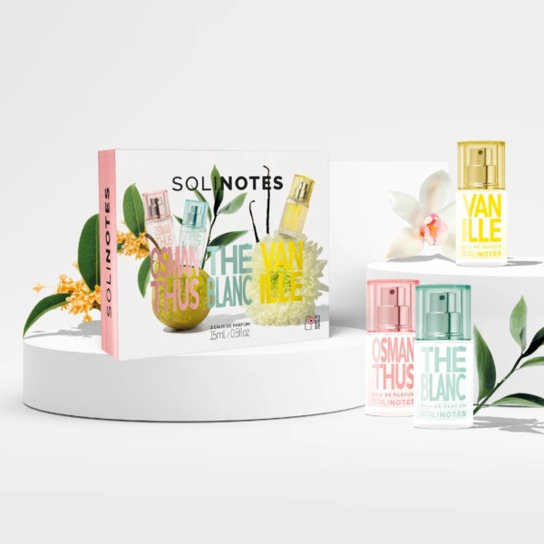 Solinotes Coffret Découverte Osmanthus Thé Blanc Vanille : trois mini-bouteilles - Osmanthus, Thé Blanc et Vanille - sont disposées à côté de leur coffret, entourées de fleurs et de fruits décoratifs sur fond blanc. Dakar