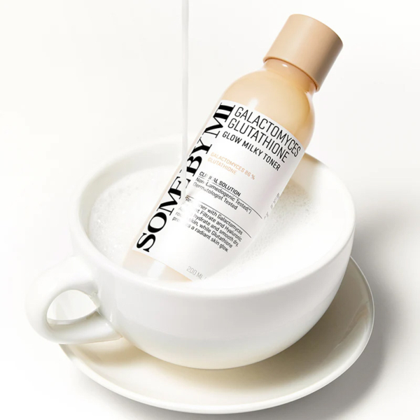 Une bouteille de Some By Mi Galactomyces Glutathione Glow Milky Toner reposant dans une tasse à thé blanche remplie de lait mousseux, le lait étant versé dans la tasse. Dakar
