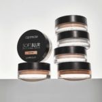 Cinq récipients ronds de Catrice Poudre Fixatrice Mate Soft Blur 8 g, teinte 040 Tan, sont empilés sur le côté à côté d'un récipient tourné vers l'avant pour présenter l'étiquette et le couvercle noir du produit. Dakar
