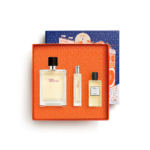 Un coffret cadeau Hermès orange à pois blancs contient trois parfums Terre d'Hermès : un grand flacon, un vaporisateur de voyage étroit et un petit flacon. Le couvercle de la boîte, sur lequel figure un bâtiment Hermès illustré, est placé derrière la boîte ouverte. Dakar