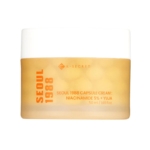 Un pot de K-Secret Seoul 1988 Capsule Cream with Niacinamide 5% and Yuja, 50 ml. Le pot est jaune givré avec un texte orange en gras et un couvercle blanc. Dakar