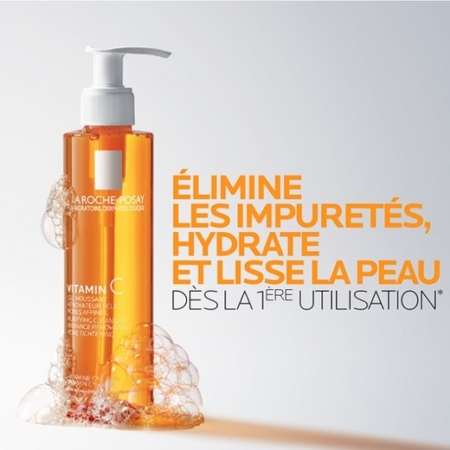 Un flacon de nettoyant à la vitamine C de La Roche-Posay avec de la mousse et des bulles autour de la base. Le texte en français se lit comme suit : "Élimine les impuretés, hydrate et lisse la peau dès la 1ère utilisation. Dakar