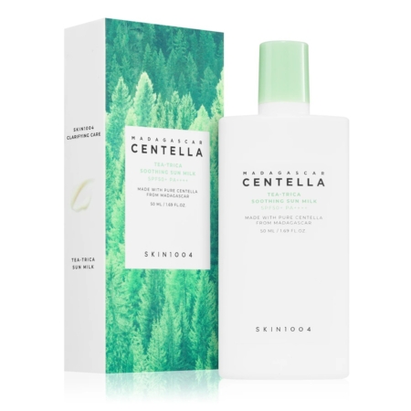 Un flacon blanc de Skin1004 Madagascar Centella Tea-Trica Soothing Sun Milk SPF50+ se trouve à côté de sa boîte, qui présente un motif de forêt verte et des détails sur le produit en vert et en texte argenté. Dakar