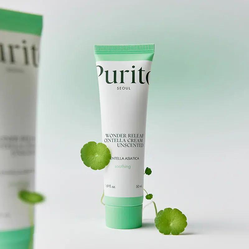 Un tube de crème Purito Wonder Releaf Centella non parfumée se tient debout, avec des feuilles vertes à côté et un fond vert clair et doux. L'étiquette met en avant ses propriétés apaisantes et l'ingrédient Centella Asiatica. Dakar