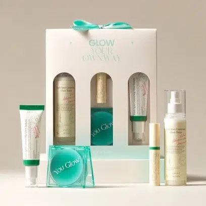 Un coffret cadeau de soins de la peau étiqueté "Glow Your Own Way" comprenant cinq produits, dont des crèmes, un spray, un tube et un récipient rond, tous avec un emballage vert clair et crème présenté sur un fond neutre. Dakar