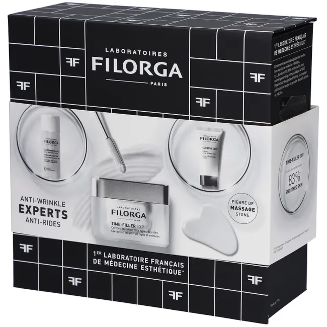 Un coffret de produits de soins Filorga Paris étiqueté "Experts anti-rides". Le coffret comprend une crème, un sérum et une pierre de massage. L'emballage est noir et blanc, avec un texte en français et les logos de la marque. Dakar
