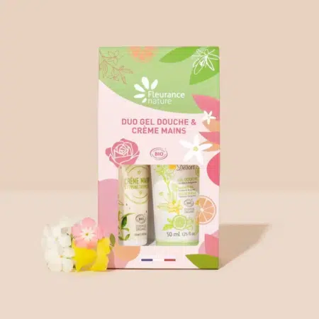 Coffret de produits Fleurance Nature, comprenant un duo de gel douche et de crème pour les mains. L'emballage est rose, vert et jaune avec des motifs floraux et d'agrumes, et une petite grappe de fleurs artificielles est placée à côté du coffret. Dakar