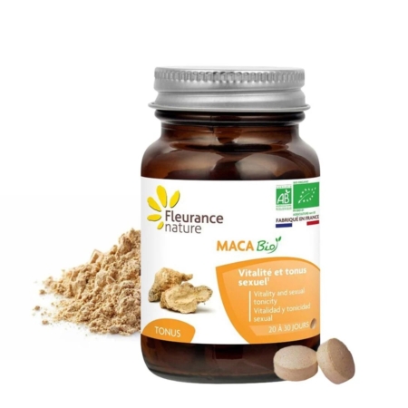 Un flacon en verre brun étiqueté "Fleurance Nature MACA Bio" avec des accents jaunes, à côté de la poudre de racine de maca et des comprimés. L'étiquette met en avant les bénéfices en termes de vitalité et d'énergie sexuelle, en français et en anglais. Dakar