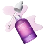 Un flacon violet de Jumiso Niacinamide 10 Serum avec un compte-gouttes est présenté. Le flacon est couché sur le côté, un peu de sérum rose s'étant répandu en dessous, et le bouchon du compte-gouttes repose sur le dessus, contenant un liquide transparent. Dakar