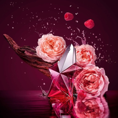 Un flacon de parfum rose en forme d'étoile est posé sur l'eau, entouré de roses roses, de framboises et d'un morceau de bois sombre, avec des éclaboussures d'eau sur un fond bordeaux foncé. Dakar