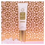 Un tube de crème pour les mains Musc Relief se tient debout sur une surface rose, avec des cristaux blancs à proximité et un fond décoratif en treillis doré. L'emballage est blanc avec des accents dorés et un texte en français. Dakar