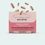 Une boîte de gélules Oxyprolane Skin Detox avec plusieurs gélules en vrac au-dessus d'elle. La boîte est rose et blanche, étiquetée pour l'anti-glycation, la purification, la désintoxication et l'anti-pollution, et contient 30 gélules. Dakar