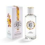 Un flacon de parfum Roger & Gallet Bois d'Orange se trouve à côté de son coffret blanc, tous deux ornés d'illustrations de fruits orange et jaunes et de touches d'or. Le flacon est muni d'un bouchon blanc et d'une étiquette ronde et décorative. Dakar