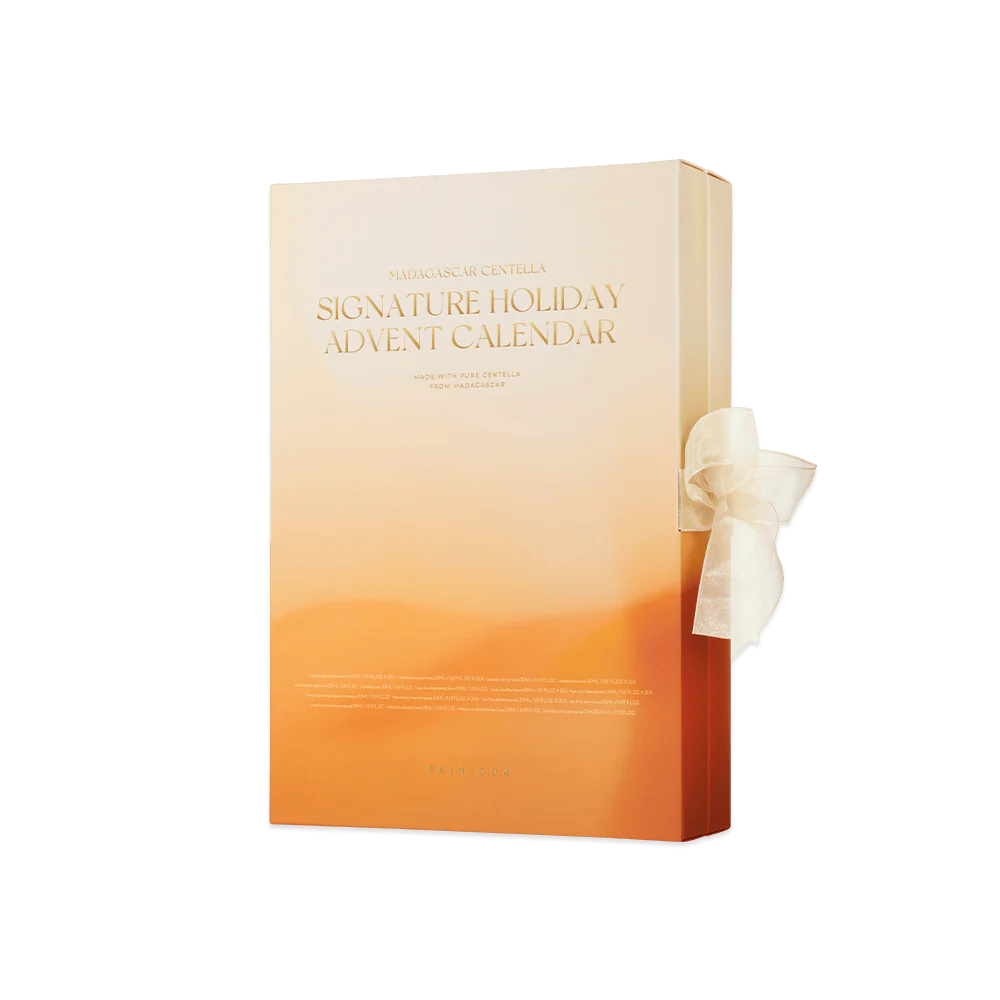 Une boîte rectangulaire orange dégradée, étiquetée "Calendrier de l'Avent Signature Holiday", avec un ruban blanc noué sur le côté droit, sur un fond vert uni. Dakar