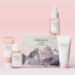 Quatre produits Skin1004 Kit de Voyage Centella de Madagascar Anti Pores Dilates sont disposés sur une surface rose avec une boîte présentant un graphique de montagne. L'emballage rose et blanc comprend des flacons, un tube et un flacon compte-gouttes. Dakar