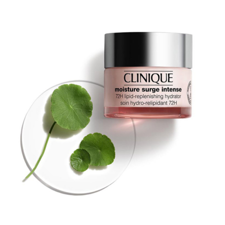 Un pot de crème Clinique Moisture Surge Intense est posé à côté d'un plat en verre contenant trois feuilles vertes, le tout sur fond blanc. Le pot est rose pâle, avec un couvercle argenté et une étiquette transparente. Dakar