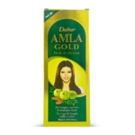 Une boîte jaune et verte de 300 ml (10.14 fl oz) d'huile capillaire Dabur Amla Gold Huile de Cheveux montre une femme aux cheveux longs et raides, des fruits d'amla verts, et des détails multilingues sur le produit. Dakar